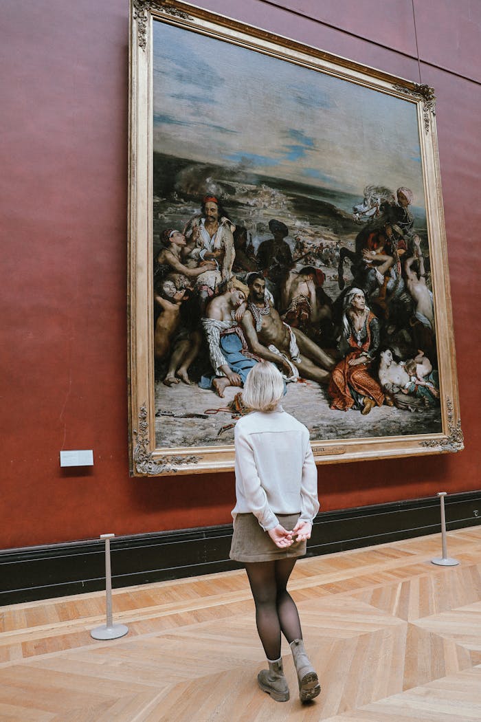 Services A woman admires a large historic painting in a museum, showcasing fine art appreciation.