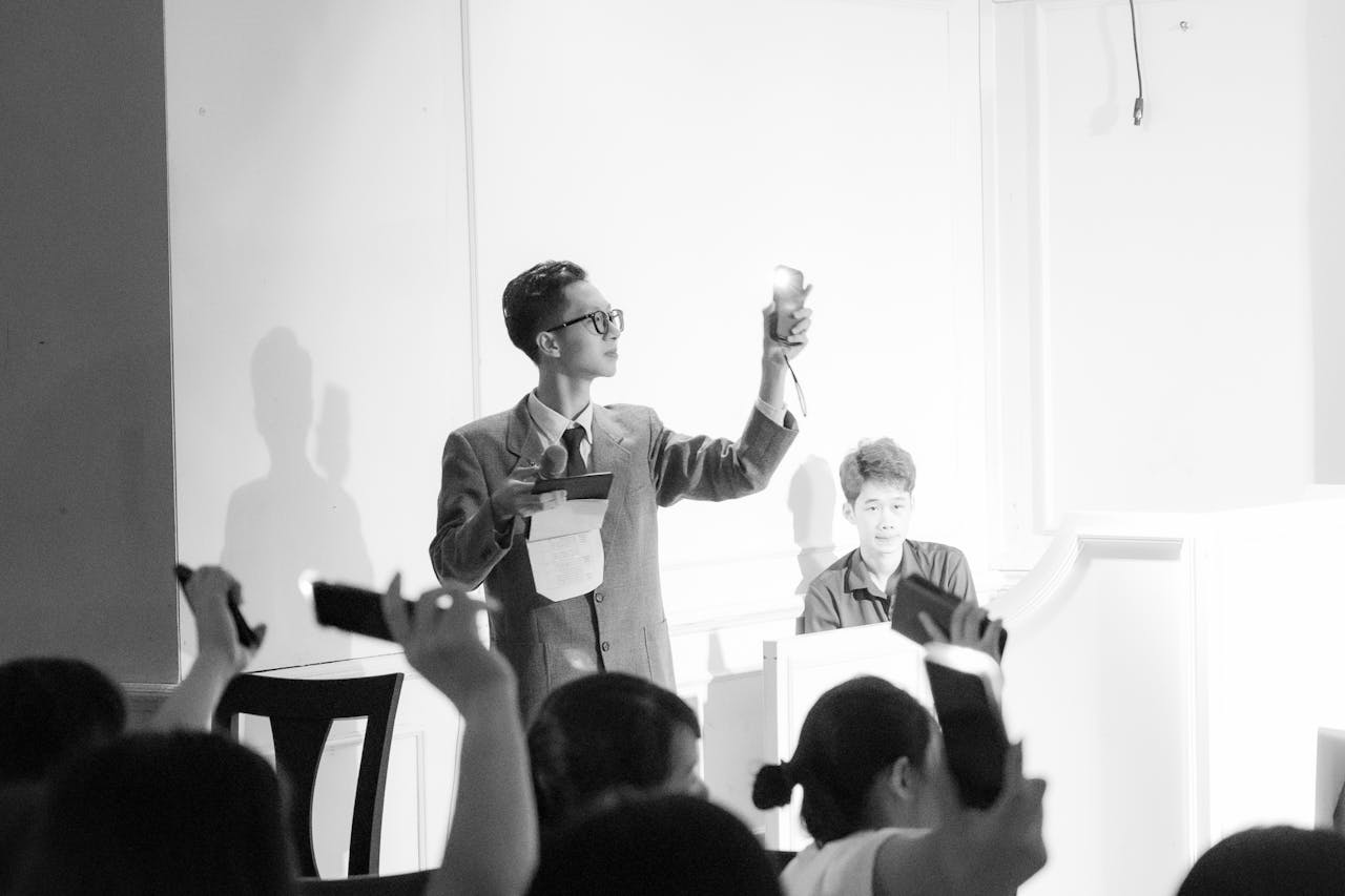 Home Elegant black and white photo of an auction scene with a presenter and bidders raising phones.