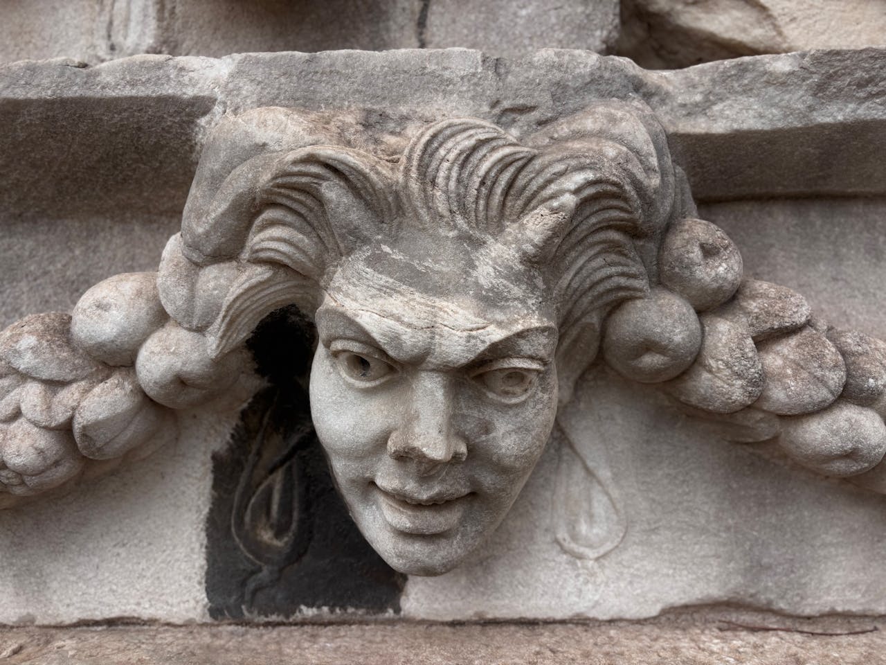 About Close-up of a detailed stone gargoyle sculpture with an expressive face and intricate hair. Architectural detail.
