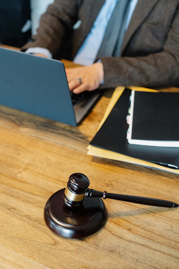 Home From above of crop anonymous male lawyer in formal clothes typing on laptop while sitting at wooden table with stack of documents and gavel