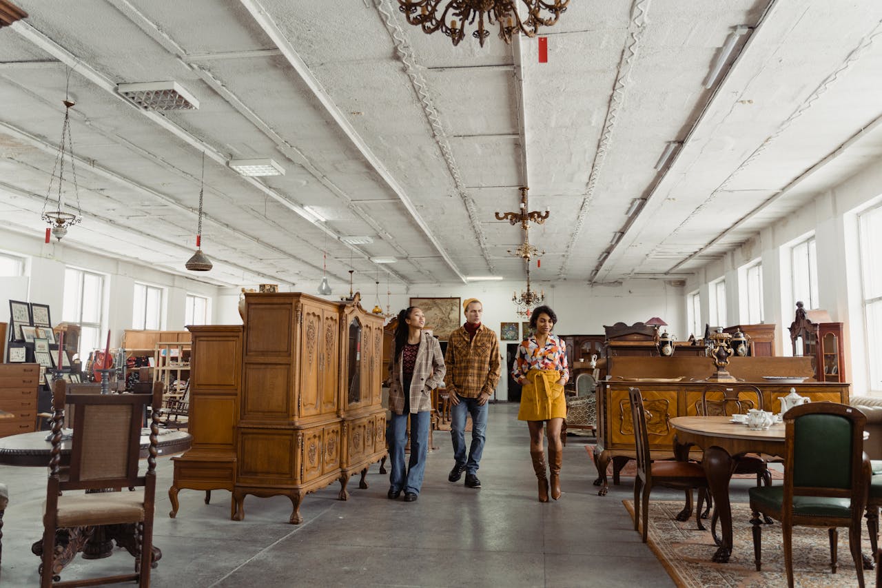 Contact Three adults exploring a spacious vintage furniture showroom filled with wooden pieces.
